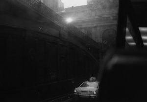 Cover image for “Falling Action in Hoboken” by Lucy Tan, featuring a black and white photo of a car driving away down the street.