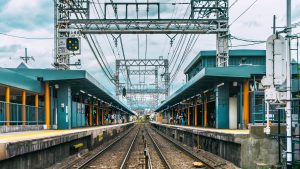 Cover image for “To the Train Station Fortuneteller” by Daniel Tam-Claiborne, featuring a train station against a blue sky with white clouds.