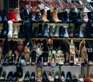 Cover image for "in ache" by Melissa Llanes Brownlee, featuring four rows of heeled boots and shoes.